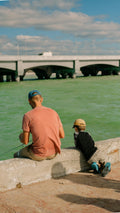 A man and a boy are sitting on a wall by the water
