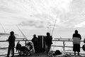 People are fishing off a pier in monochrome.