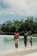 Three people are fishing in the shallow water.