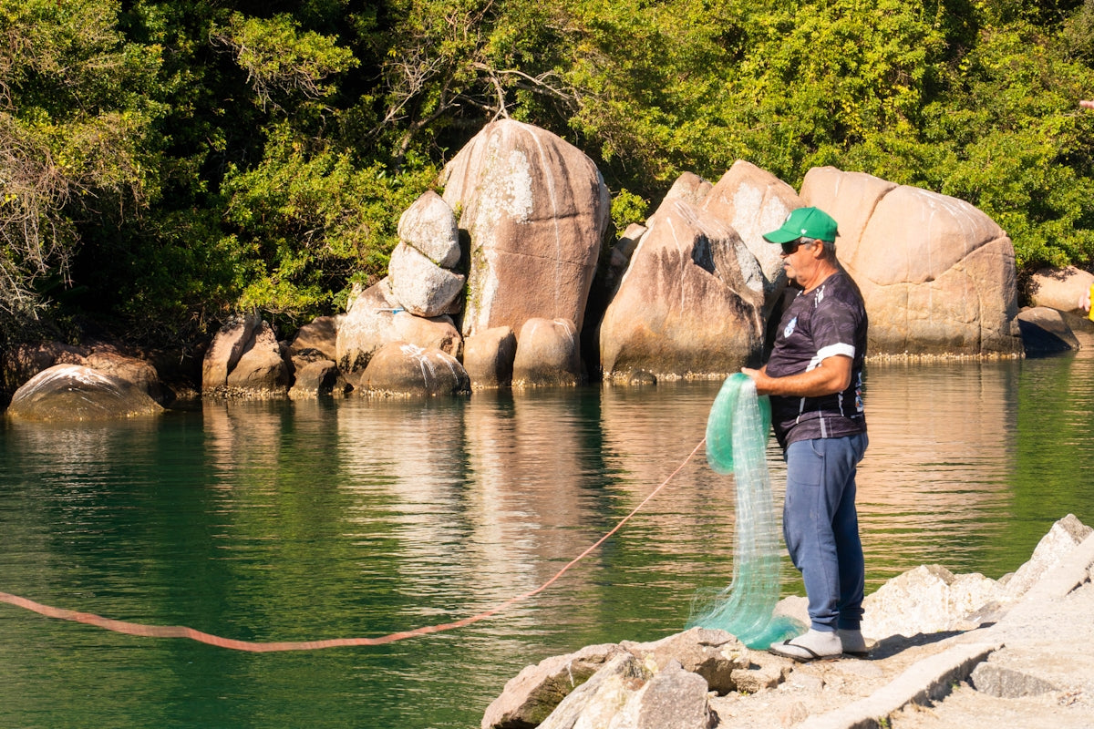 A man fishing near water using a 60m Fishing Net Buoy Anchor 2.5kg Dan Combo.
