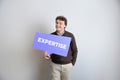 Smiling man holds a purple expertise sign.