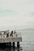 People fishing with rods on a concrete pier overlooking the calm sea