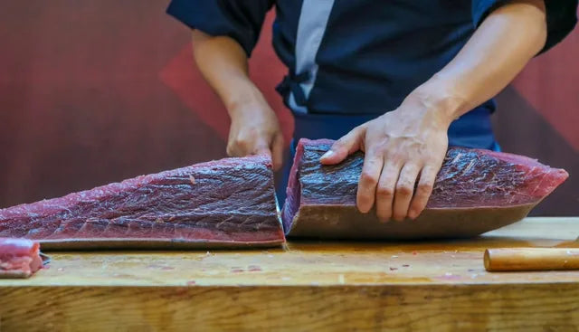 Person cutting raw fish on a wooden board with a blurred background
