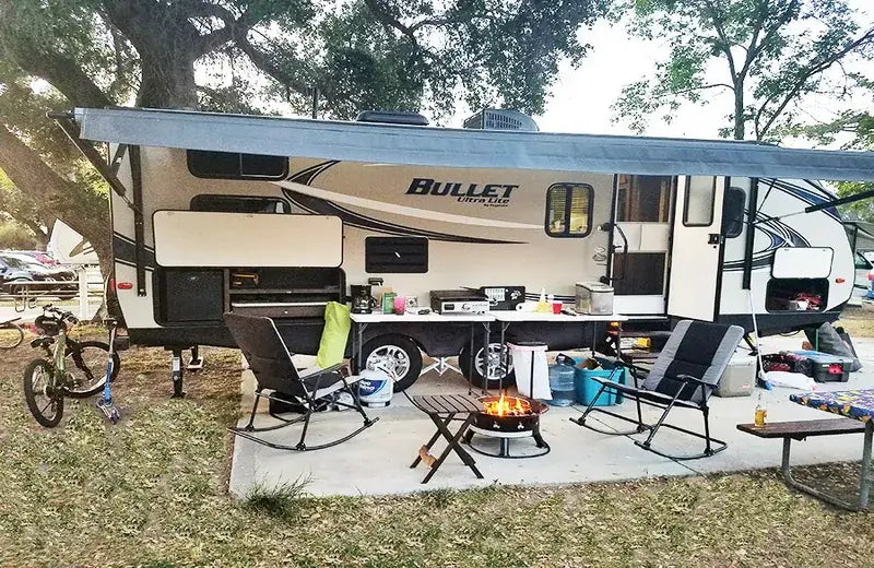 Outdoor setup with Bullet camper, chairs, and a fire pit in a park-like setting.