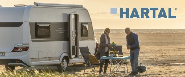 Couple enjoying outdoor cooking with Hartal Doors on their camper by the beach during sunset. Product Spotlight Hartal Doors.