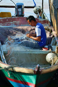 A fisherman on a boat working with dark green long line twine while repairing fishing nets.