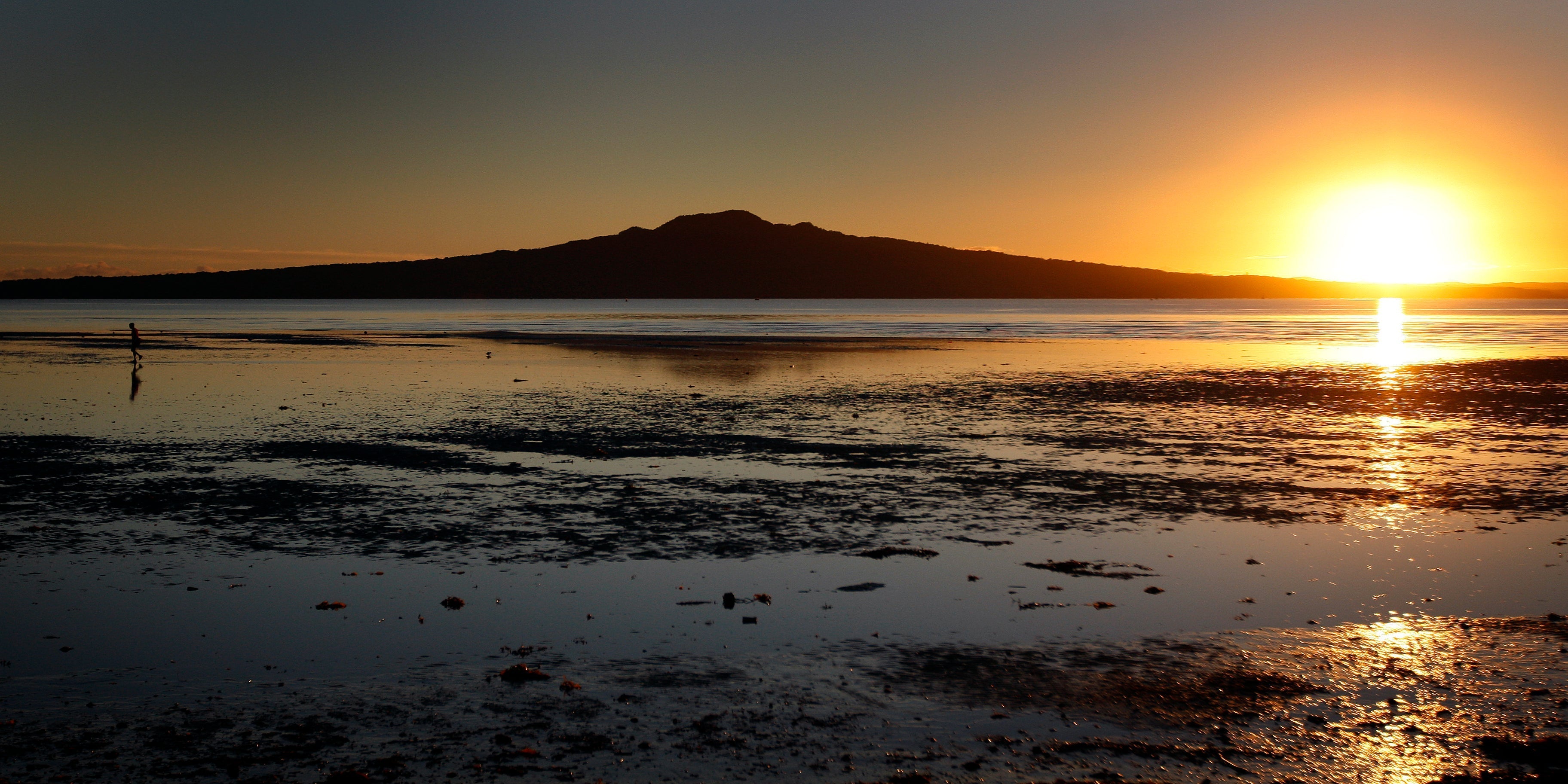 Sunset over a calm bay reflecting a mountain, showcasing serene nature and coastal beauty.