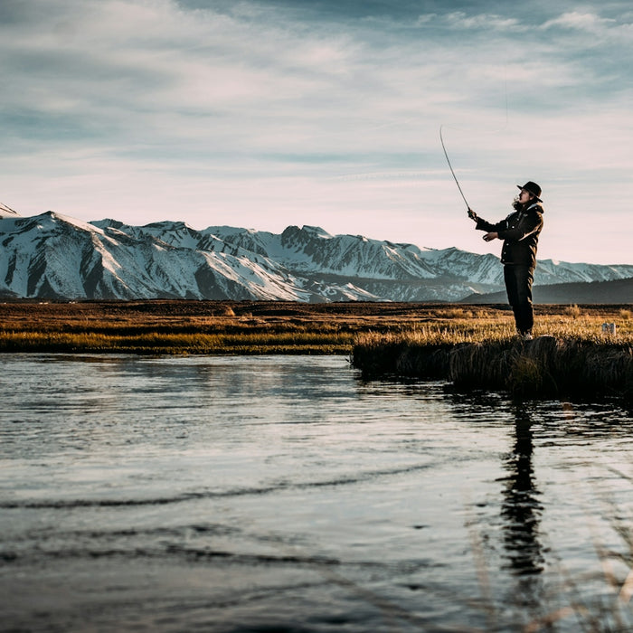 landscape photo of man fishing on river near mountain alps