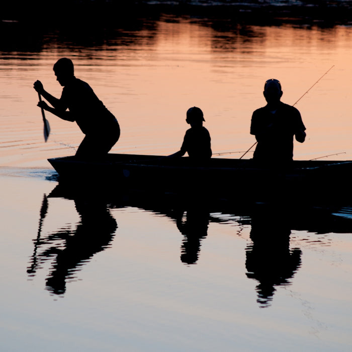 silhouette of three person riding on boat on body of water