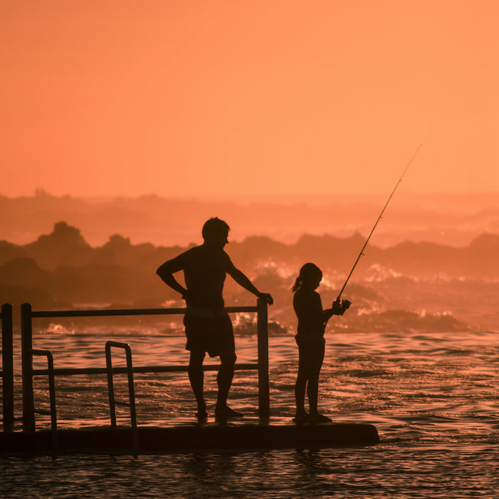 silhouette of man and girl fishing during sunset