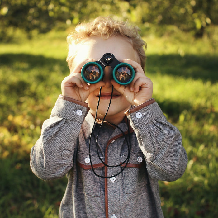 child standing while using green binoculars