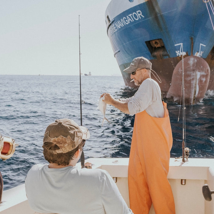 two person in fishing boat near cargo ship during daytime