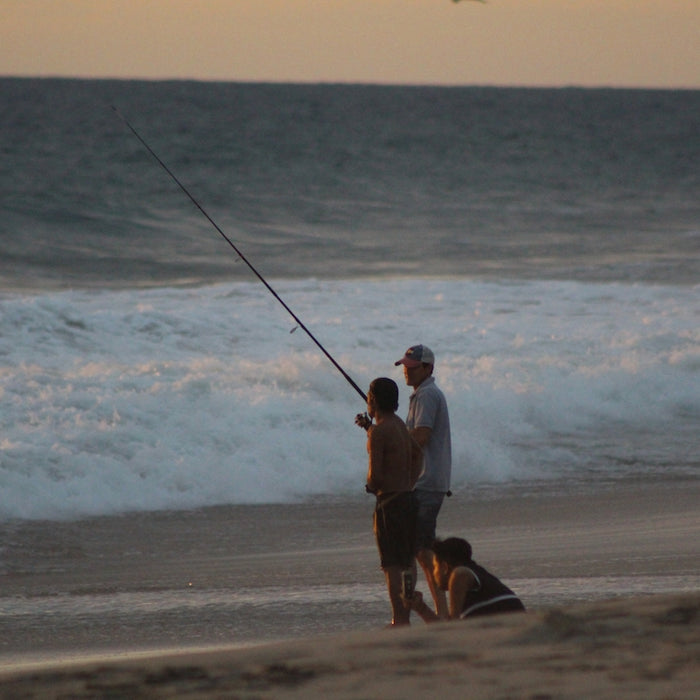 man and woman holding fishing rods walking on beach during daytime