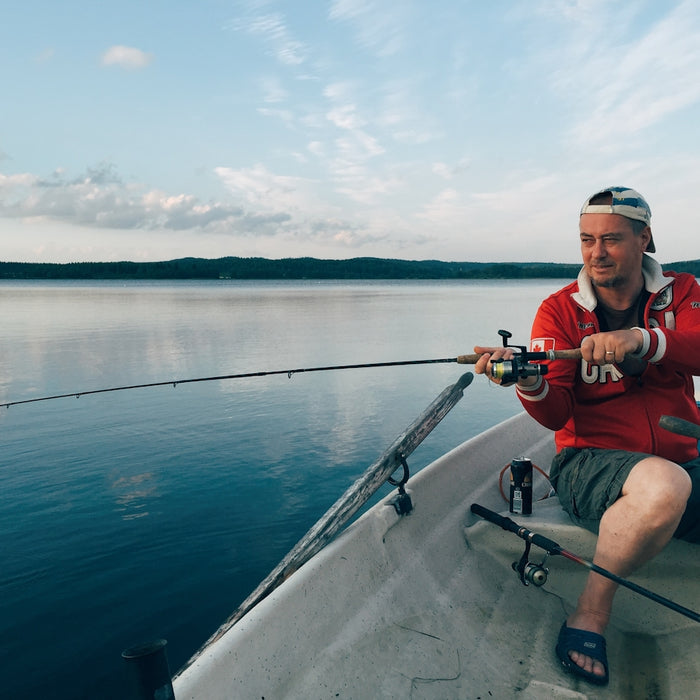 man in red shirt and black shorts sitting on boat holding fishing rod during daytime