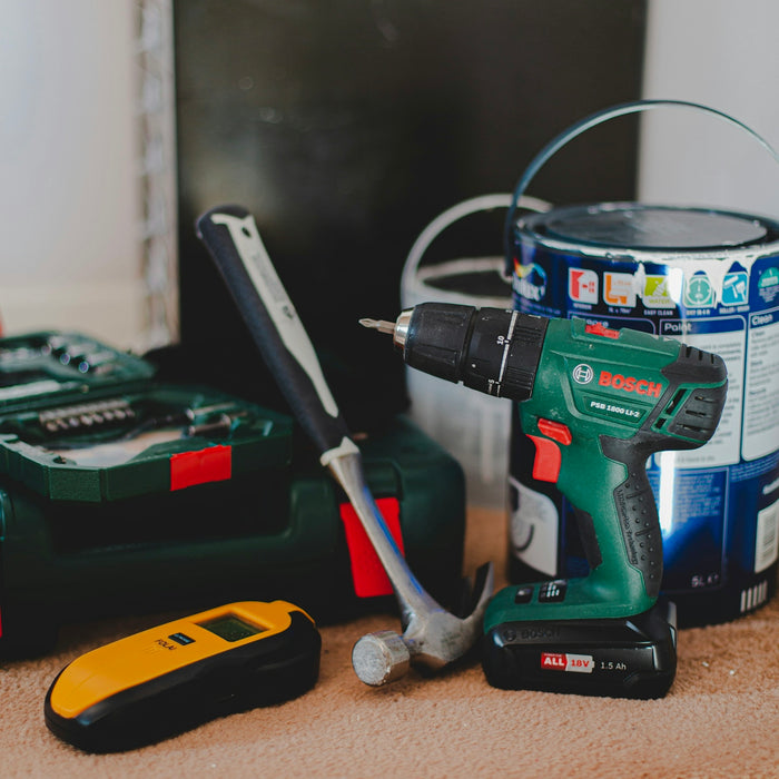 A cordless drill, a hammer, and a yellow stud finder on a carpeted floor
