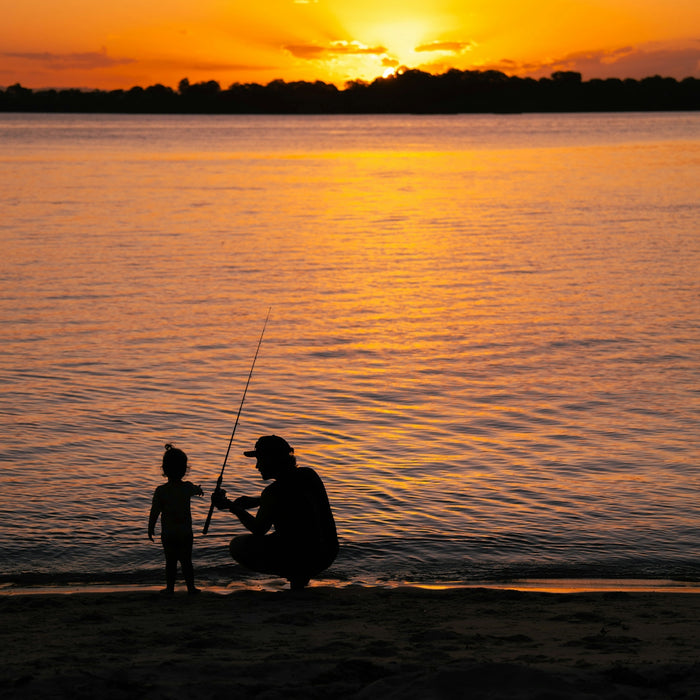 a father and son fishing on the beach at sunset