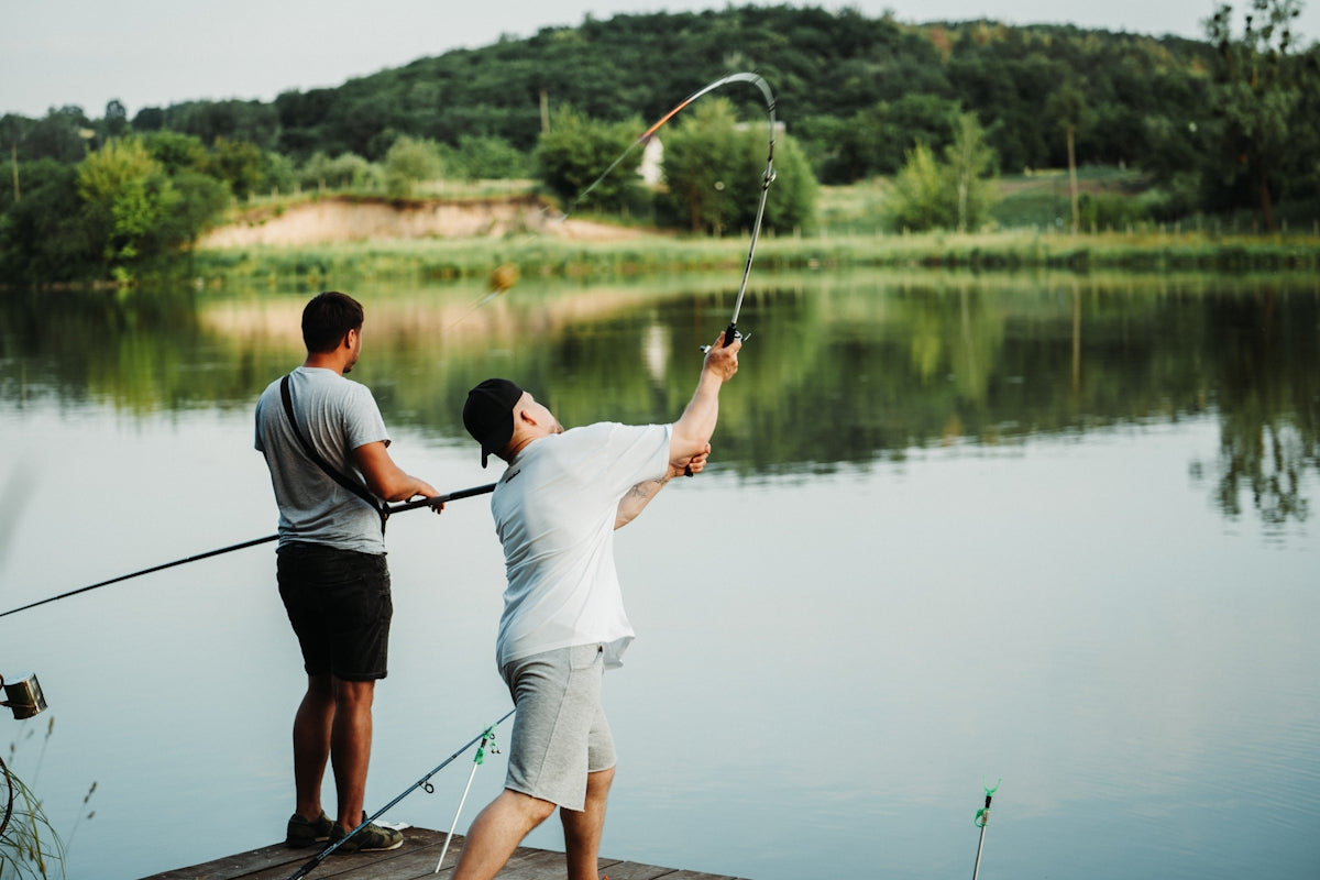 a couple of men standing on top of a pier next to a lake