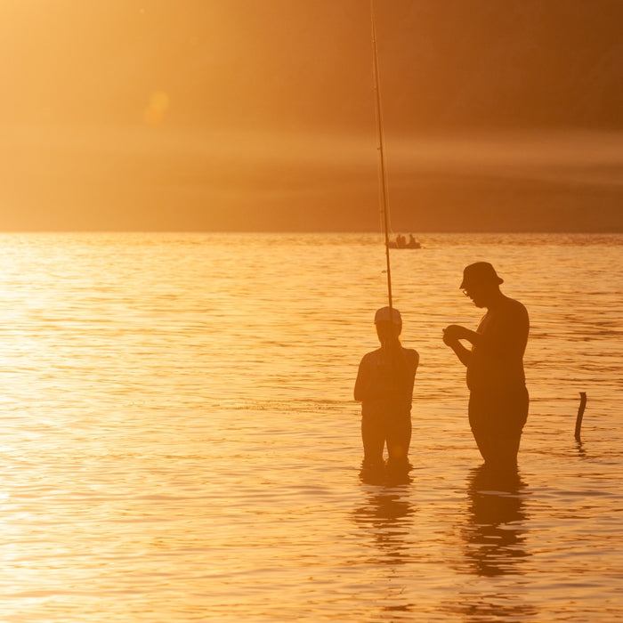 a father and son fishing in the lake at sunset