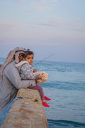 a woman and a child are sitting on a wall by the water
