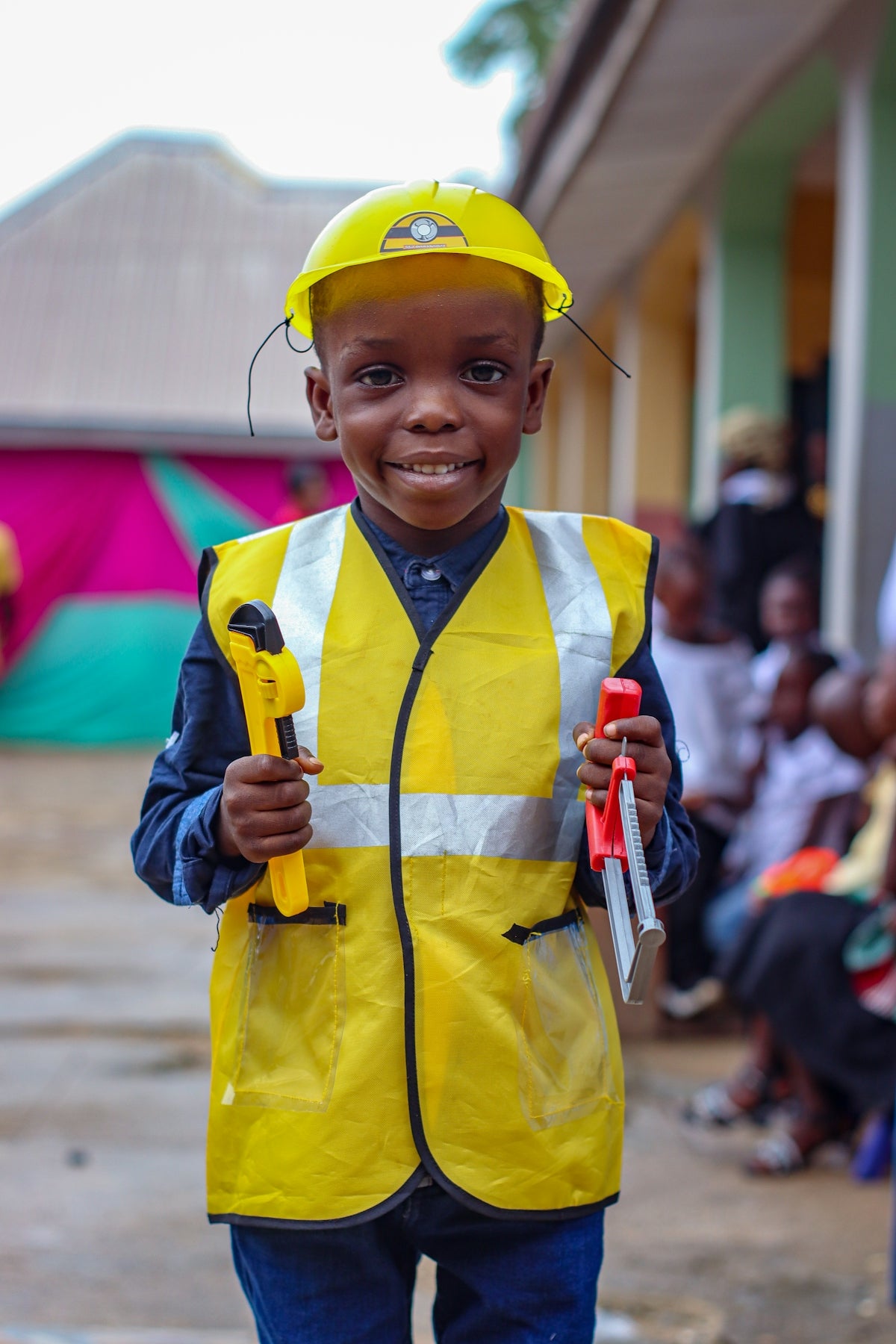 A young boy wearing a safety vest and holding a tool