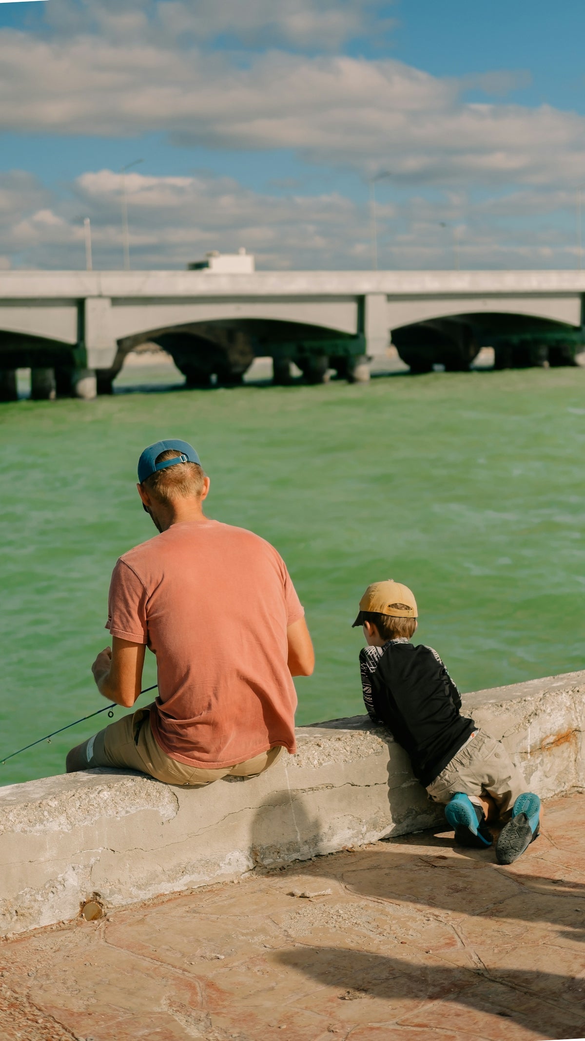 A man and a boy are sitting on a wall by the water