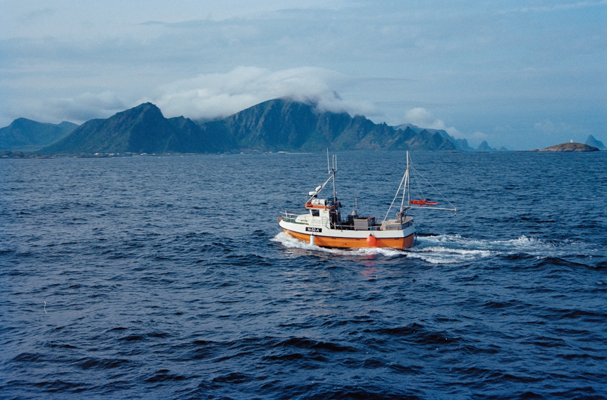 A boat sails on the sea, mountains in the background.