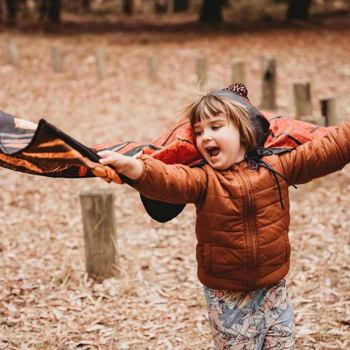 A young child runs outdoors holding a blanket