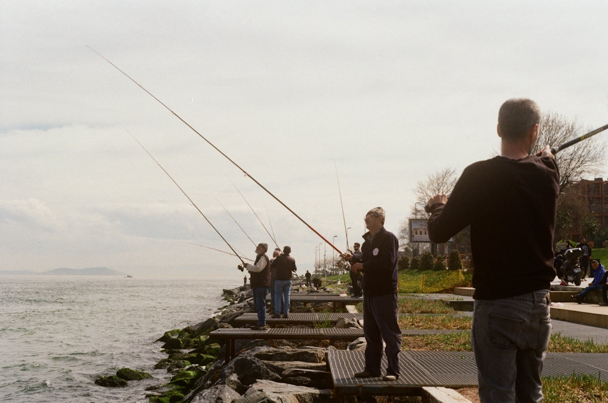 People fishing from a rocky shore on a cloudy day.