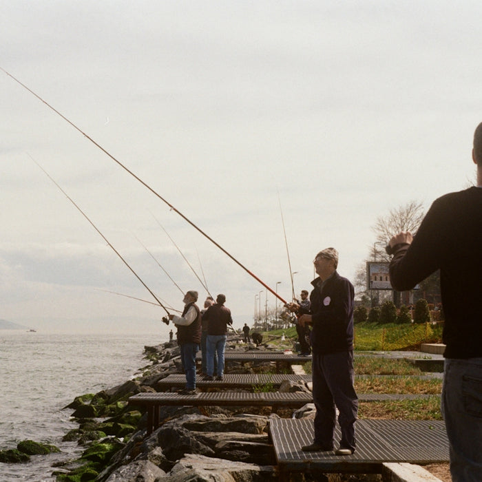 People fishing from a rocky shore on a cloudy day.