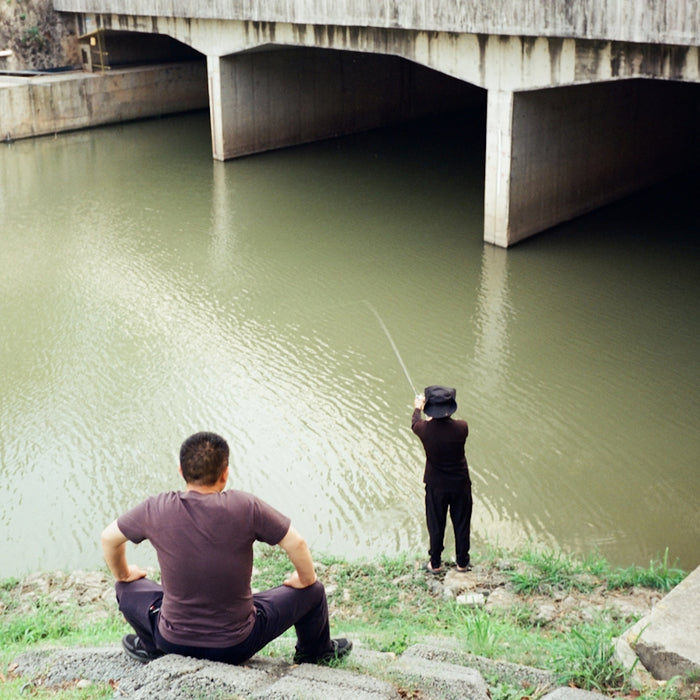 Two people fishing under a concrete bridge.
