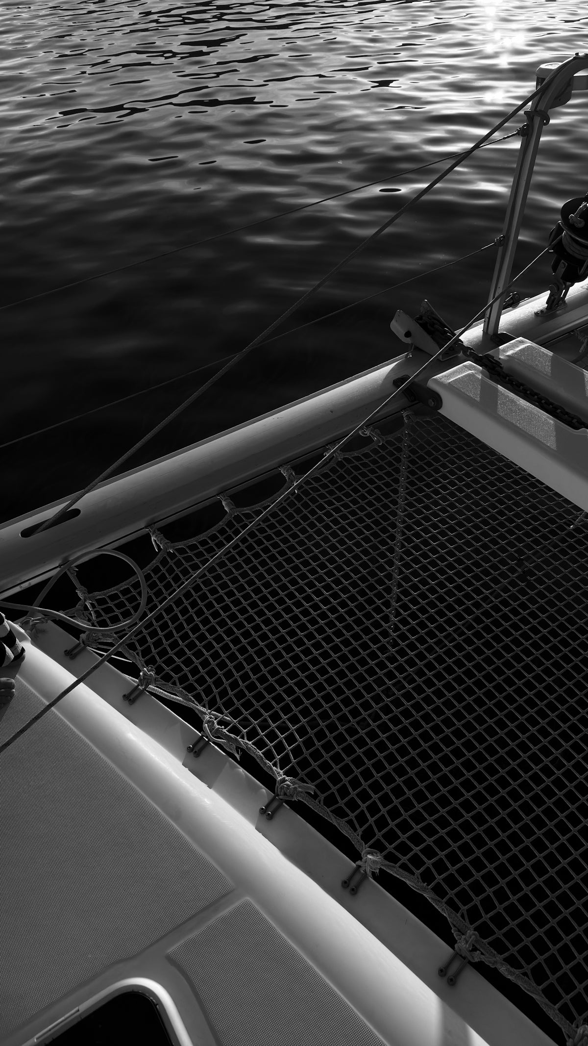 Catamaran bow with netting over sparkling water, black and white