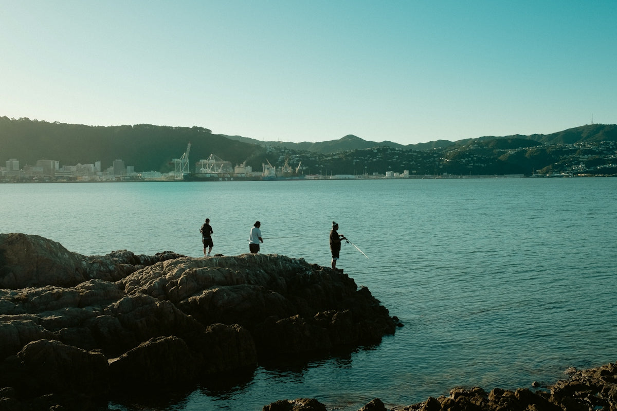 Three people fishing on rocks by a calm bay