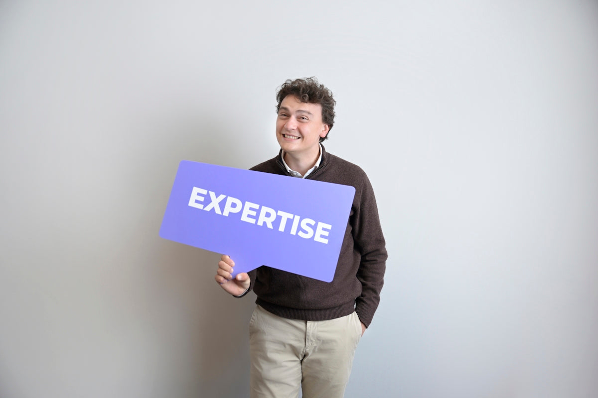 Smiling man holds a purple expertise sign.