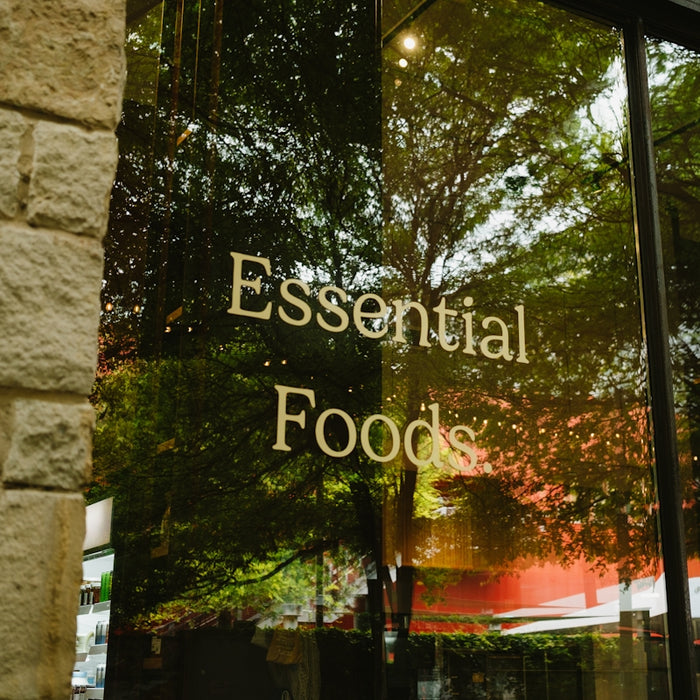 Essential foods sign on a glass window with tree reflections.