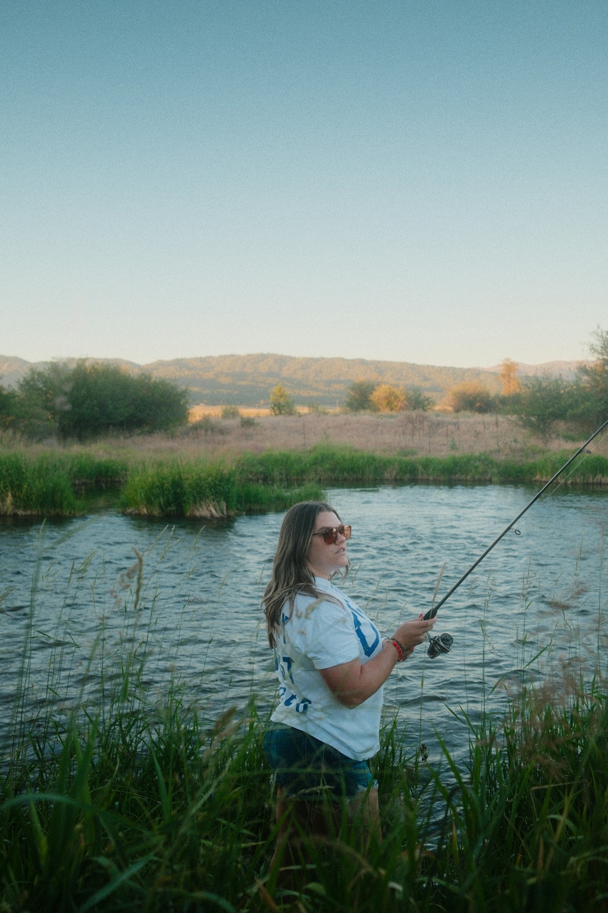 Woman fishing by a river surrounded by grass