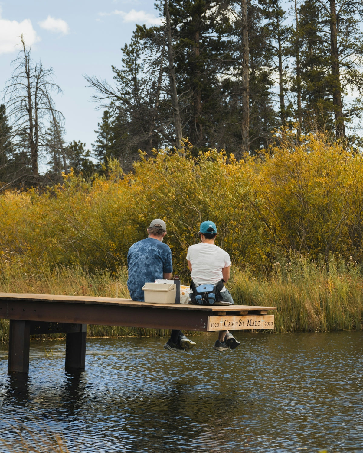Two people fishing on a dock surrounded by autumn trees