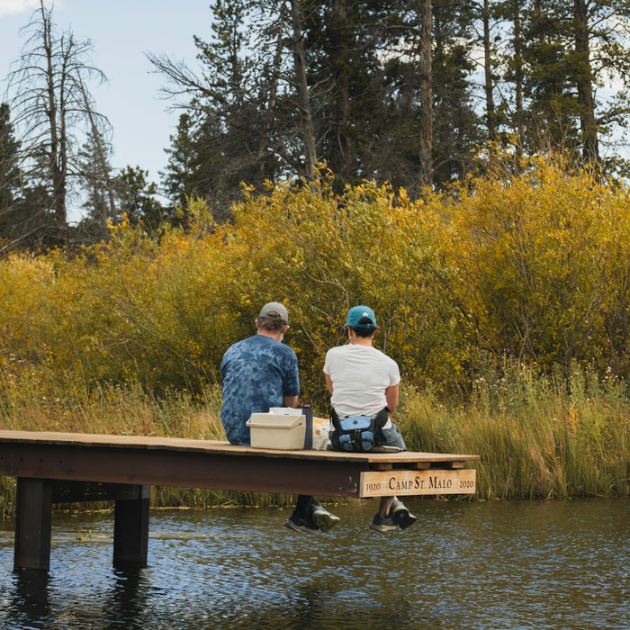 Two people fishing on a dock surrounded by autumn trees