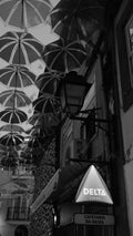 Many umbrellas suspended above a narrow street with a Delta Cafés sign