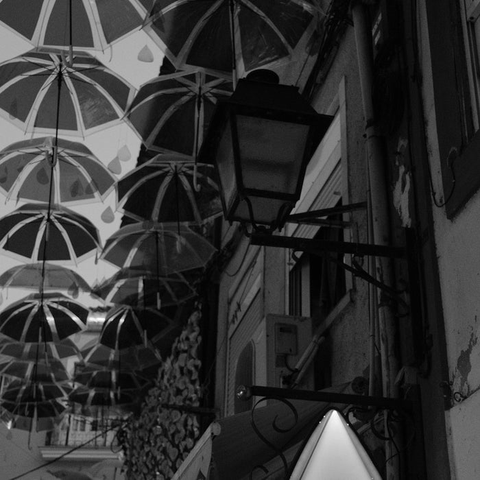 Many umbrellas suspended above a narrow street with a Delta Cafés sign