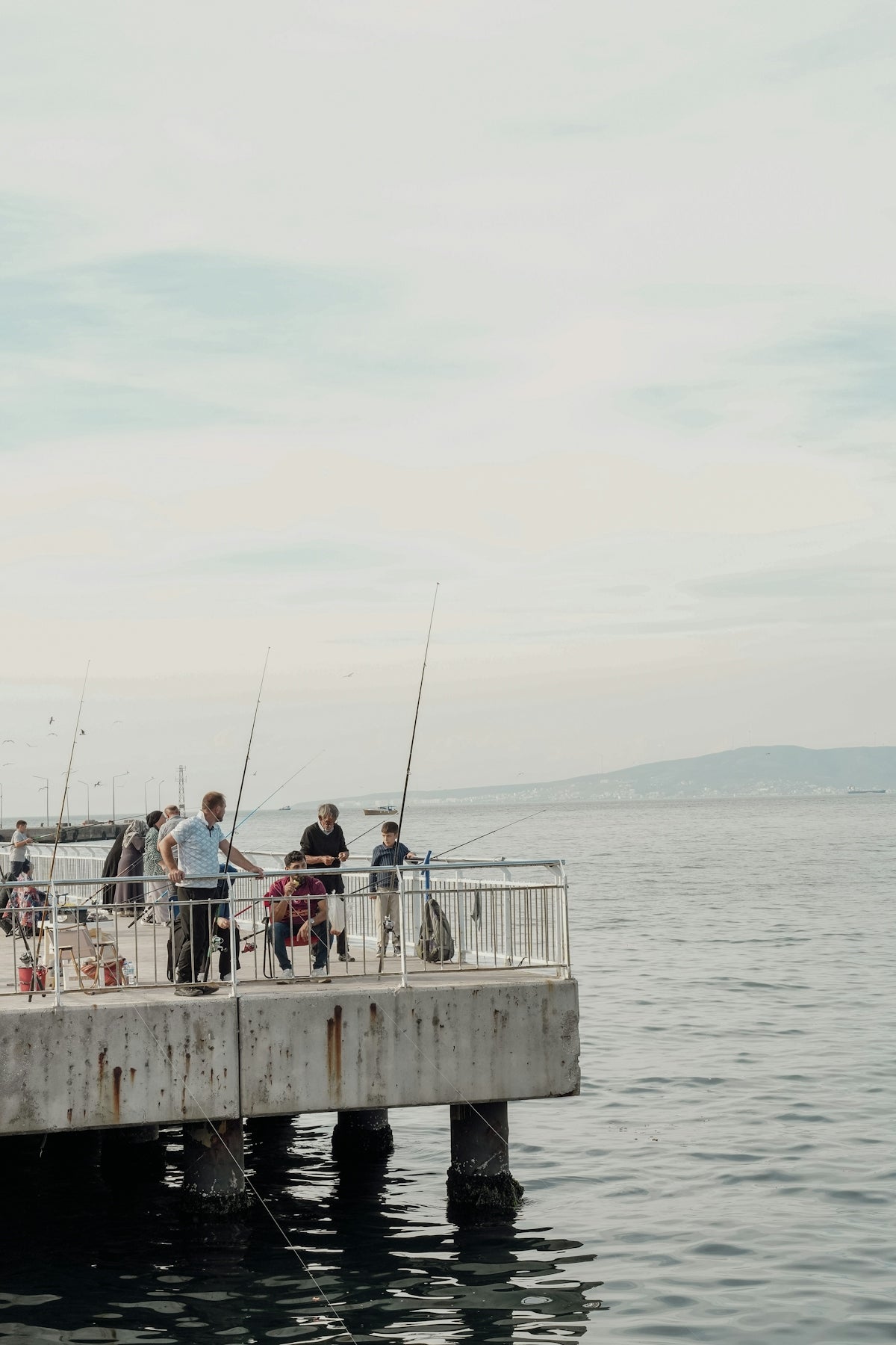 People fishing with rods on a concrete pier overlooking the calm sea