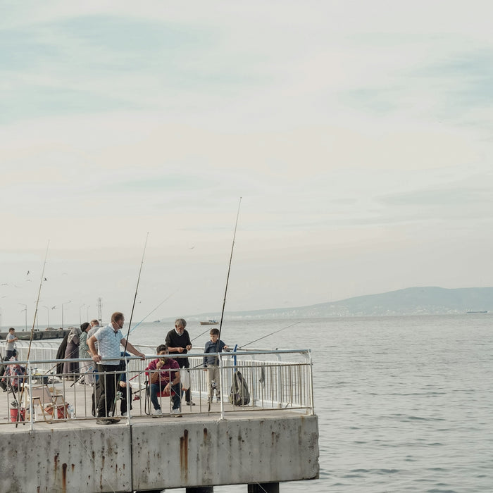 People fishing with rods on a concrete pier overlooking the calm sea