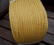 Powerdan 3 strand 220m Rope - A close-up of sturdy yellow rope coiled on a wooden surface.