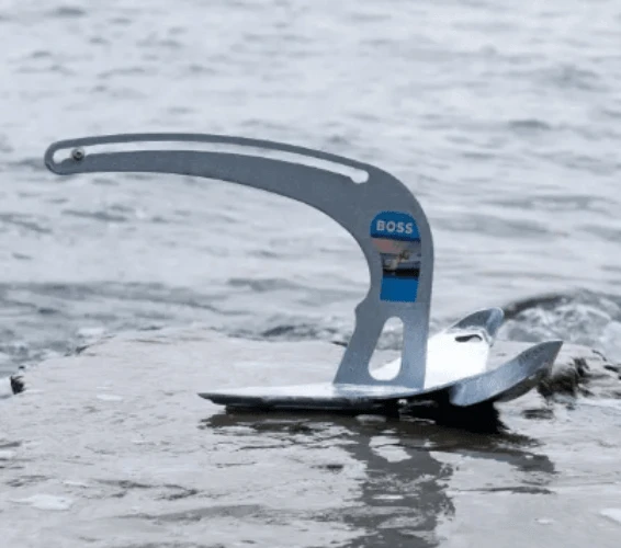 Manson Boss Anchor resting on a rocky surface by the water, showcasing its unique design and durability.