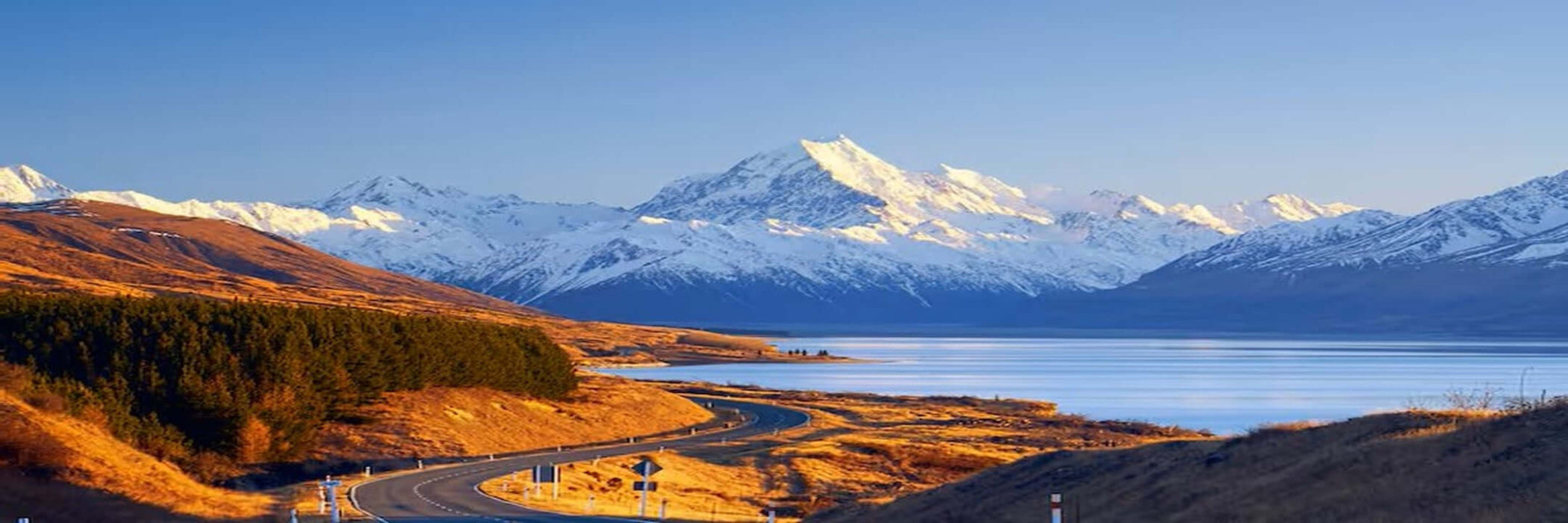 Scenic view of a mountain range with snow peaks, a lake, and a winding road.