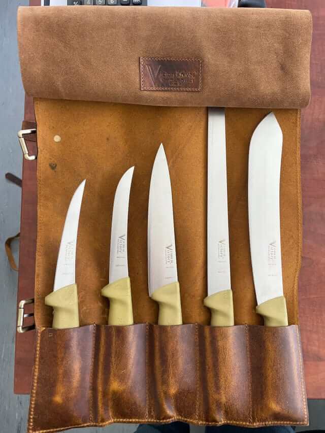 Butcher & BBQ Gold Knife Set displayed in a leather roll, featuring four high-quality knives with gold handles.